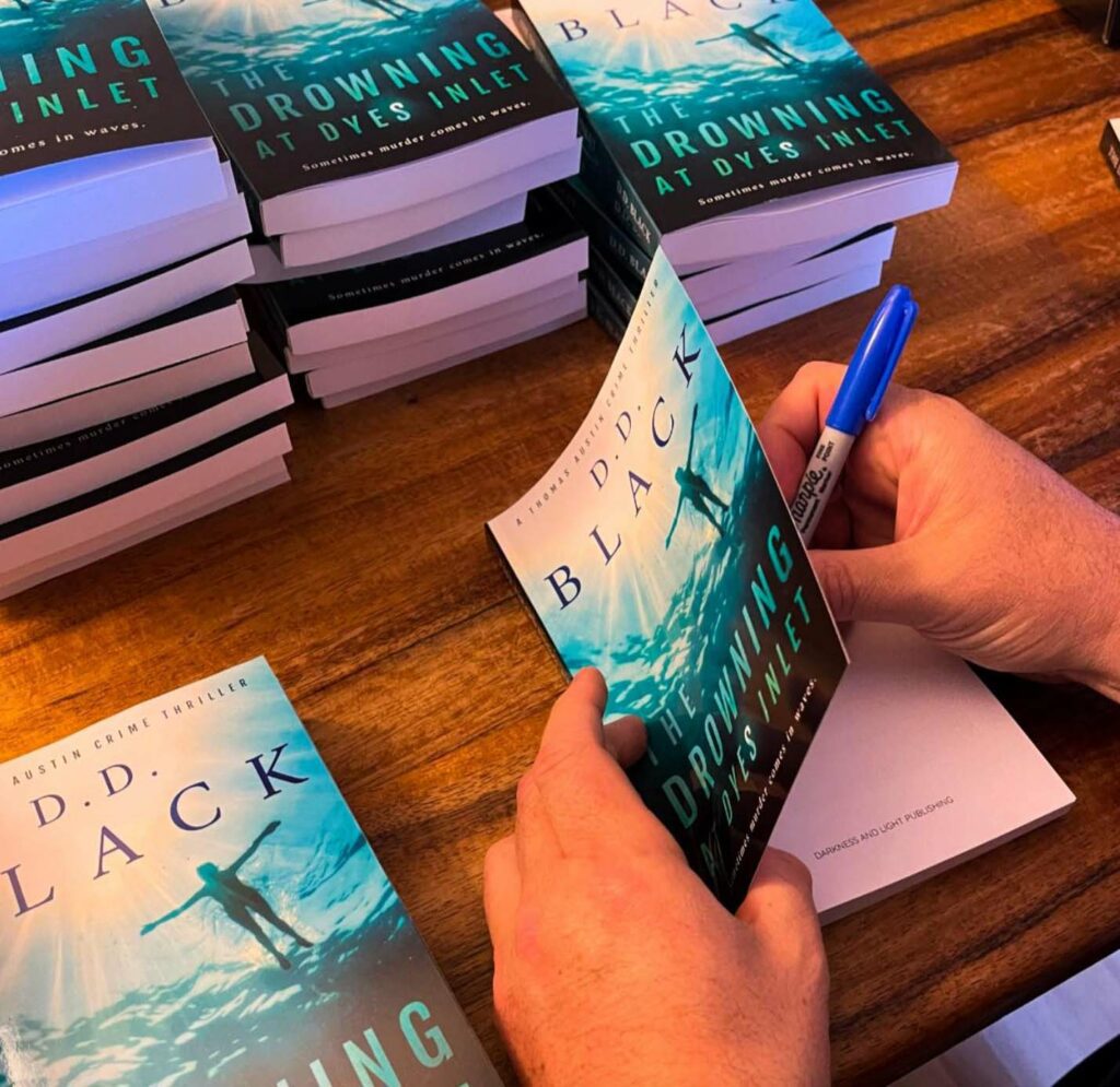 A man is writing on a book while sitting at a table.